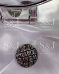 Botão metalizado com textura trançada, acabamento grafite e design rústico sofisticado.