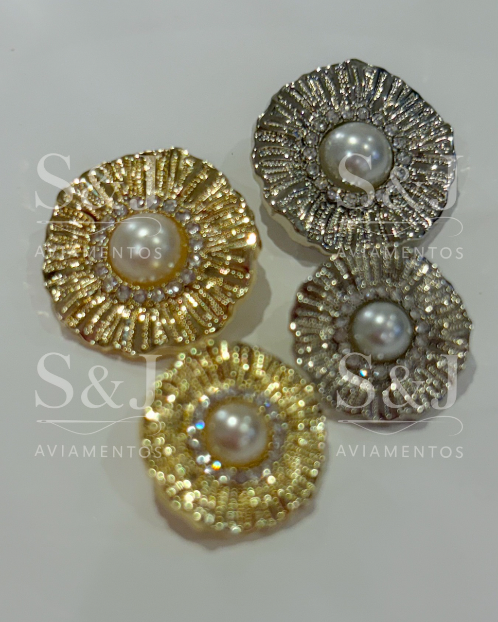 Botão sofisticado com pérola central e aro de strass, disponível em dourado e prateado